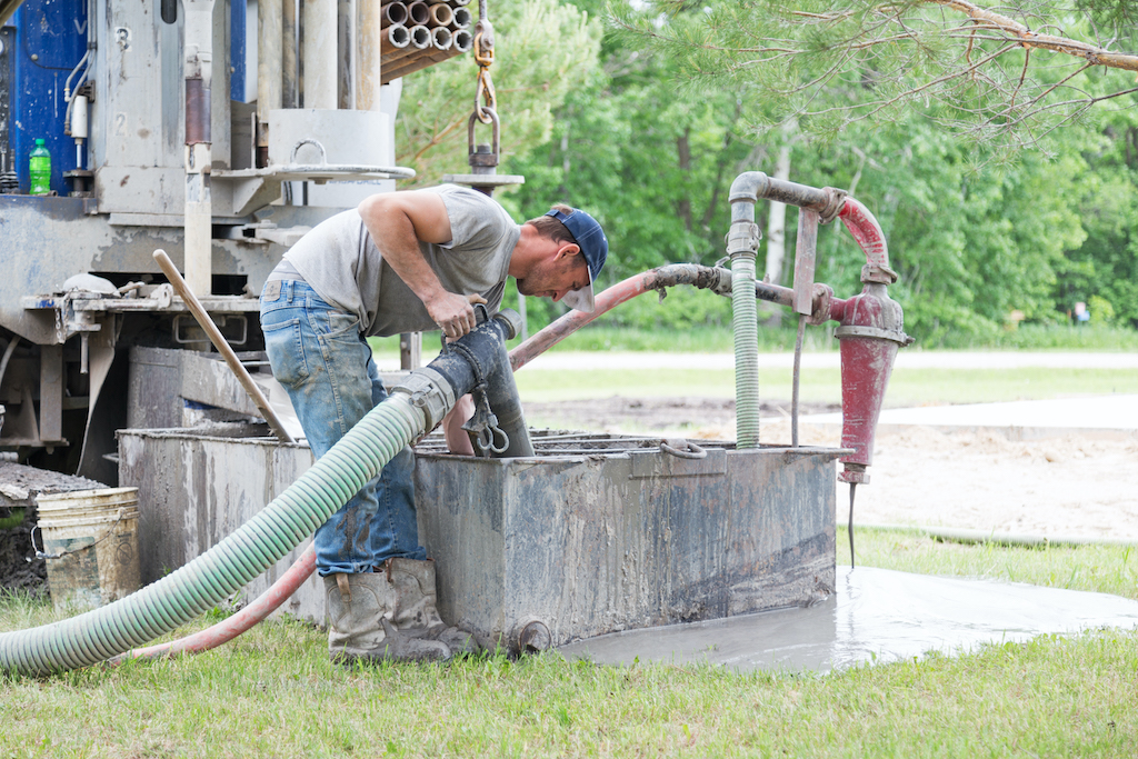Erskine, USA - May 30, 2018:  A well driller is adjusting a hose as he drills a new private residential water well.